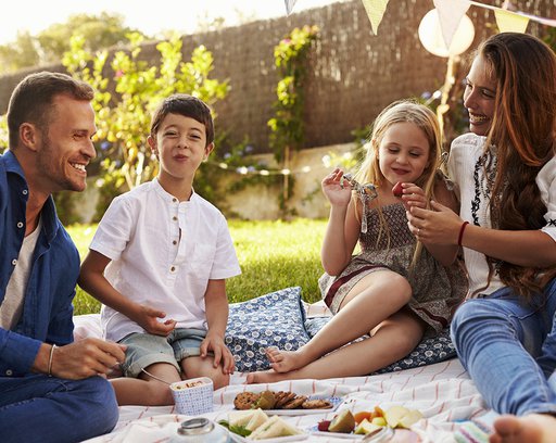 Family Enjoying Picnic On Blanket In Garden